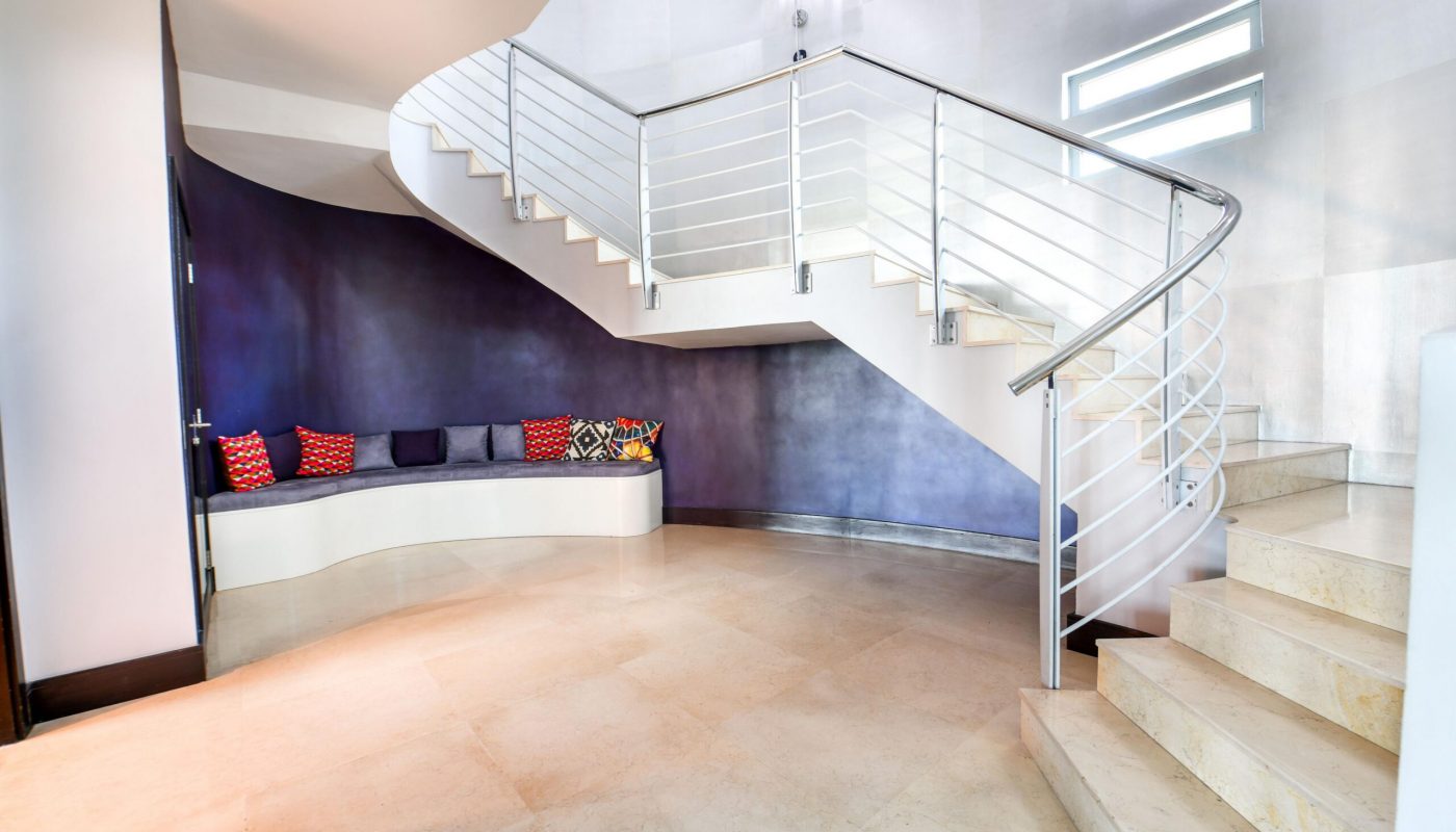 Modern interior with a curved staircase, tiled floor, built-in bench seating, and colorful patterned pillows against a dark accent wall.