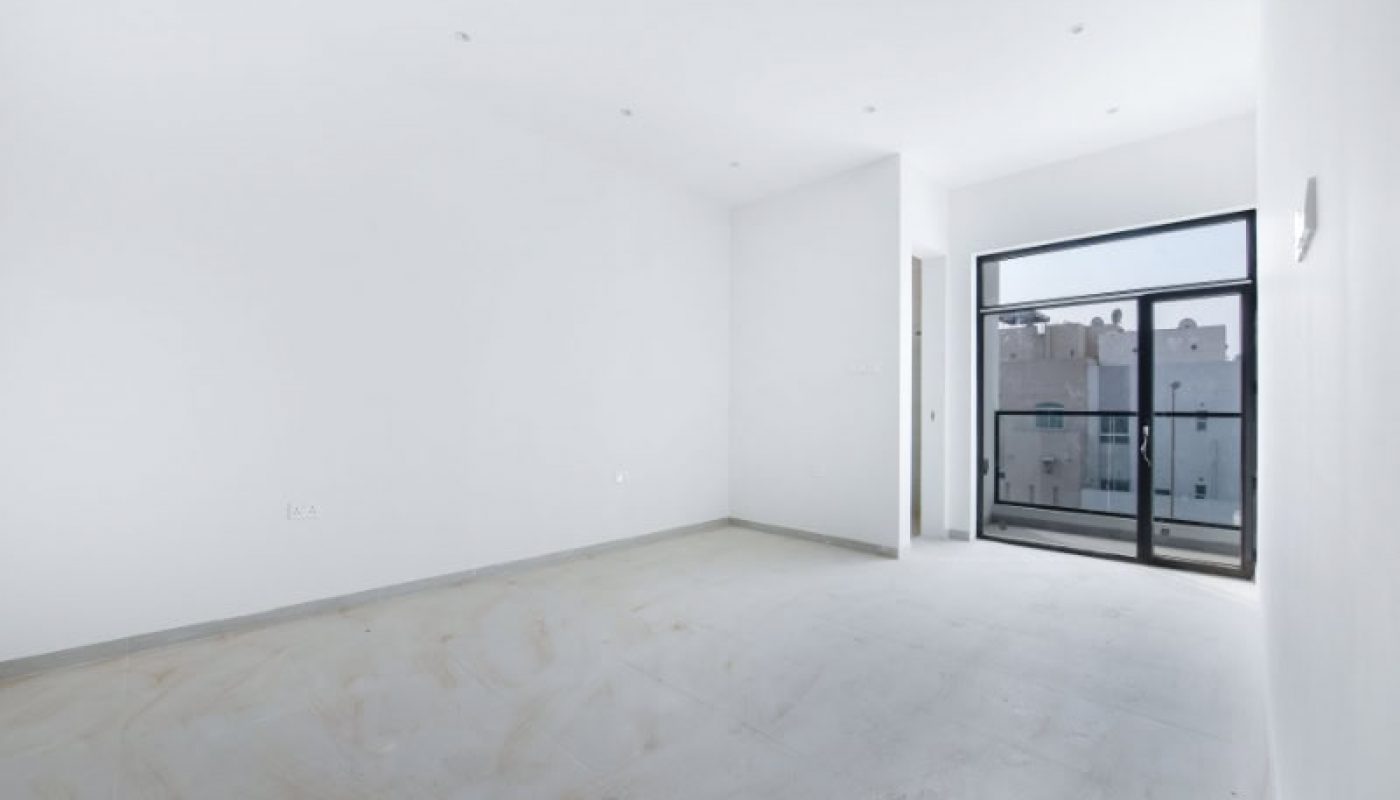 An empty, unfurnished room with white walls and tiled floor, featuring a large window with a view of building exteriors.