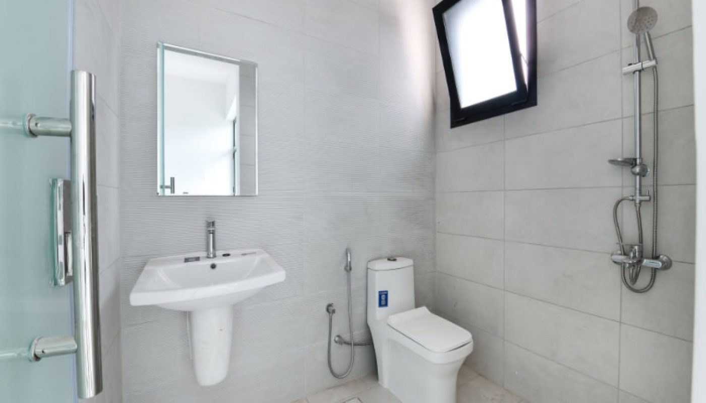 Modern bathroom with a wall-mounted sink, mirror, and toilet. A shower area is on the right with a wall-mounted showerhead. Walls and floor are tiled in light gray.