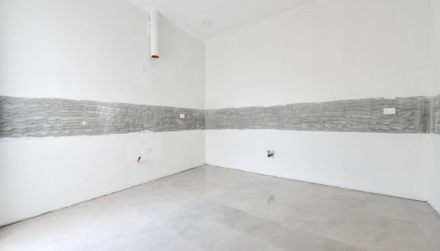 Unfinished room with tiled floor, partially plastered walls, exposed pipe, and electrical outlets.