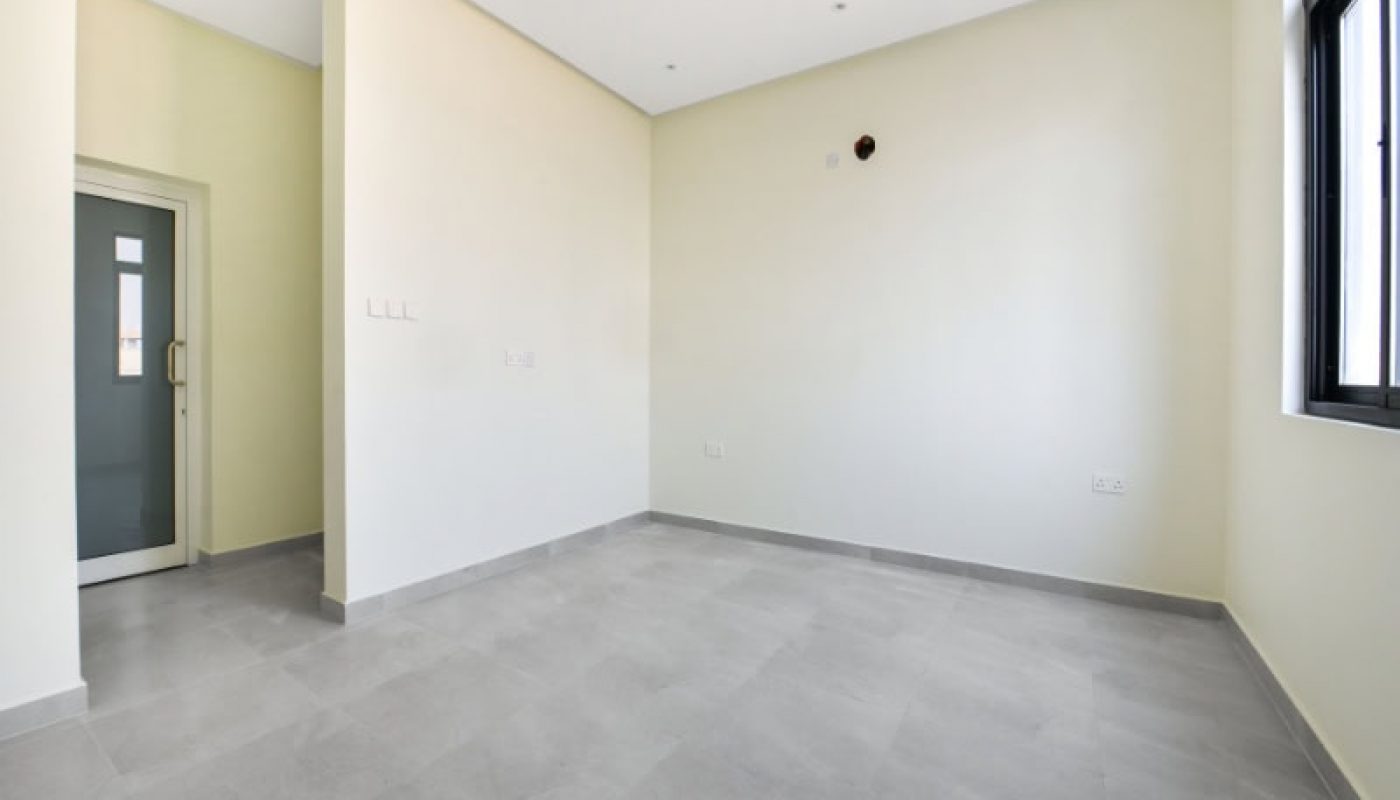 Empty room with light-colored walls and gray tiled floor, featuring a large window on the right and a glass door on the left.