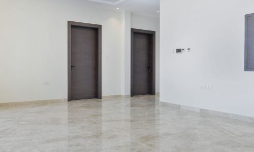 An empty room with marble floors and wooden doors, illuminated by a faint draft.