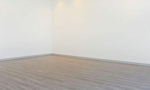 An empty room with white walls and wood floors that has an auto draft system.