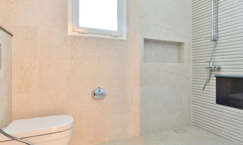 A white tiled bathroom with a toilet and shower.