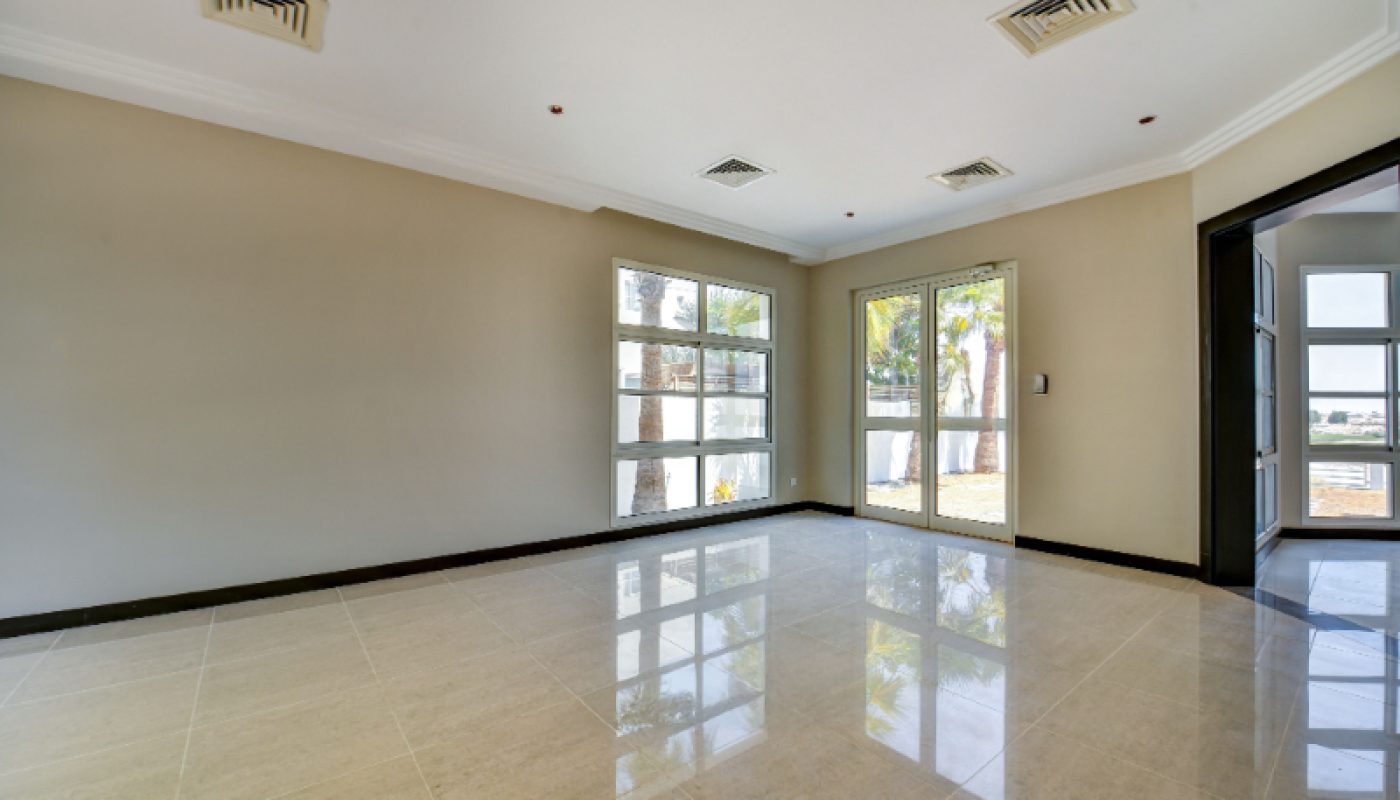 Empty room with tiled floor, beige walls, recessed ceiling lights, large windows, and a glass door leading outside. Natural light fills the space.