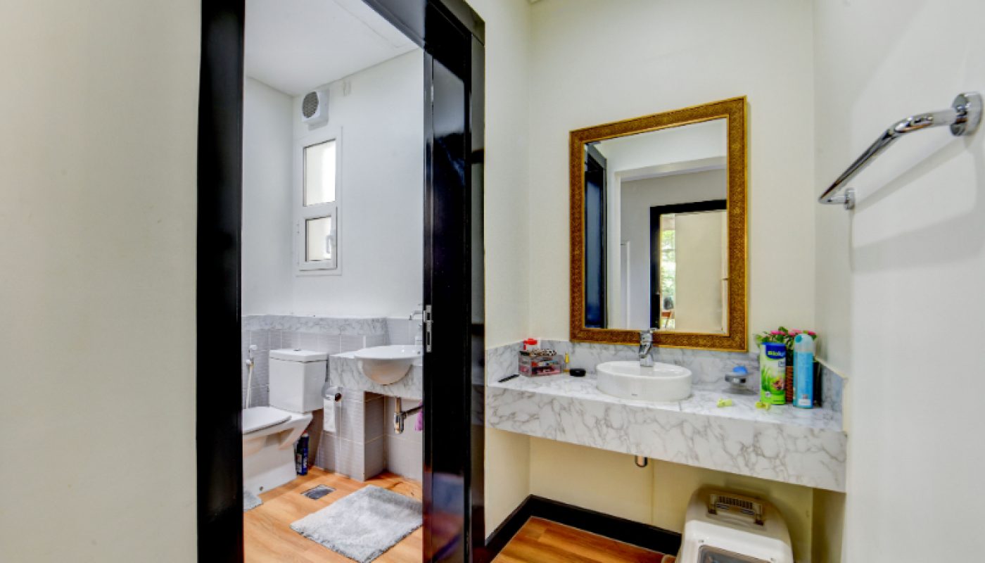A bathroom with a marble countertop, sink, and mirror; visible toiletries; adjacent room with a toilet, bidet, and small window; light walls and wood flooring.