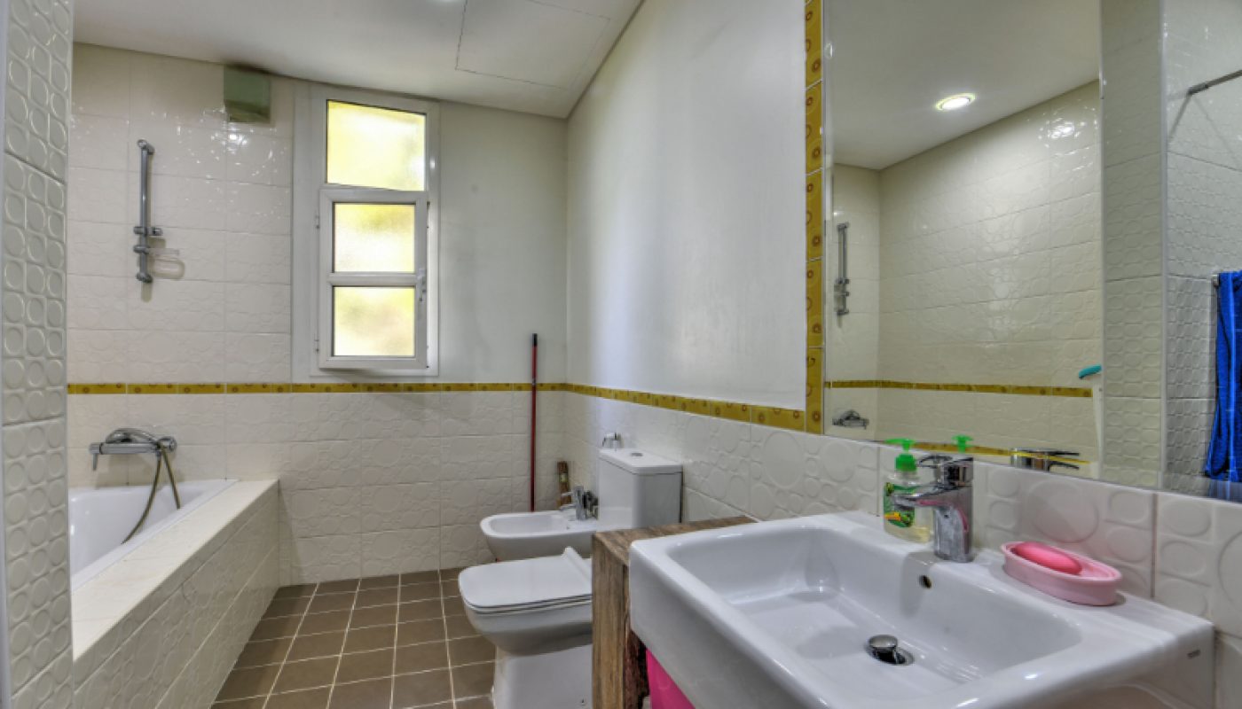 Modern bathroom with a bathtub, bidet, toilet, sink, and mirror. White tiled walls, brown floor tiles, and a window providing natural light.
