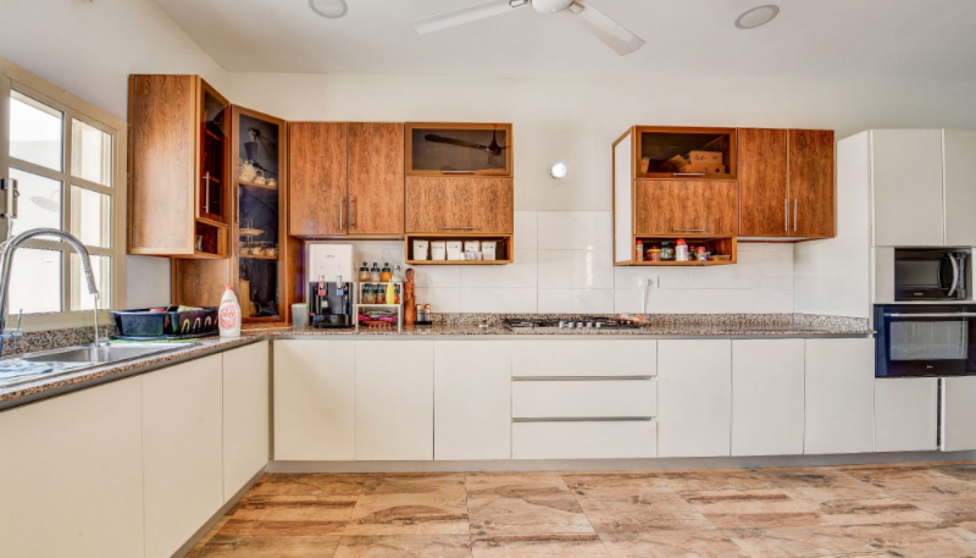 Modern kitchen with white lower cabinets, wooden upper cabinets, granite countertops, a built-in stove, oven, sink, open shelving, and ceiling fan, with natural light from a window.