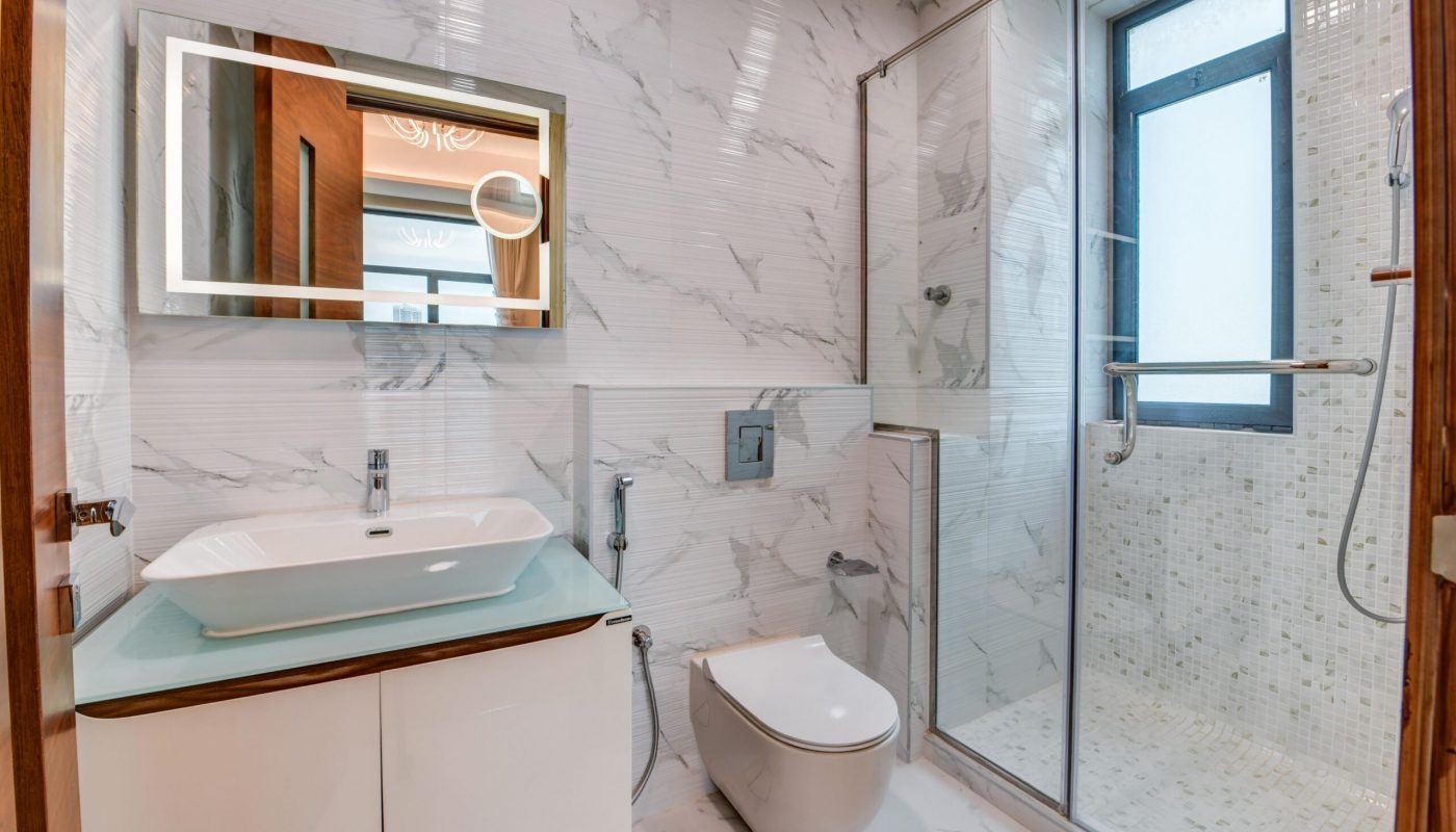 Modern bathroom with a wall-mounted sink and toilet, glass-enclosed shower, large mirror, and marble-patterned walls and floor tiles.