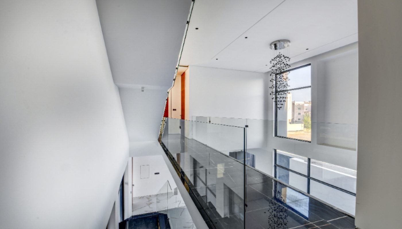 Modern interior hallway with glass railing, black tile floor, a ceiling light fixture, and large window providing natural light.