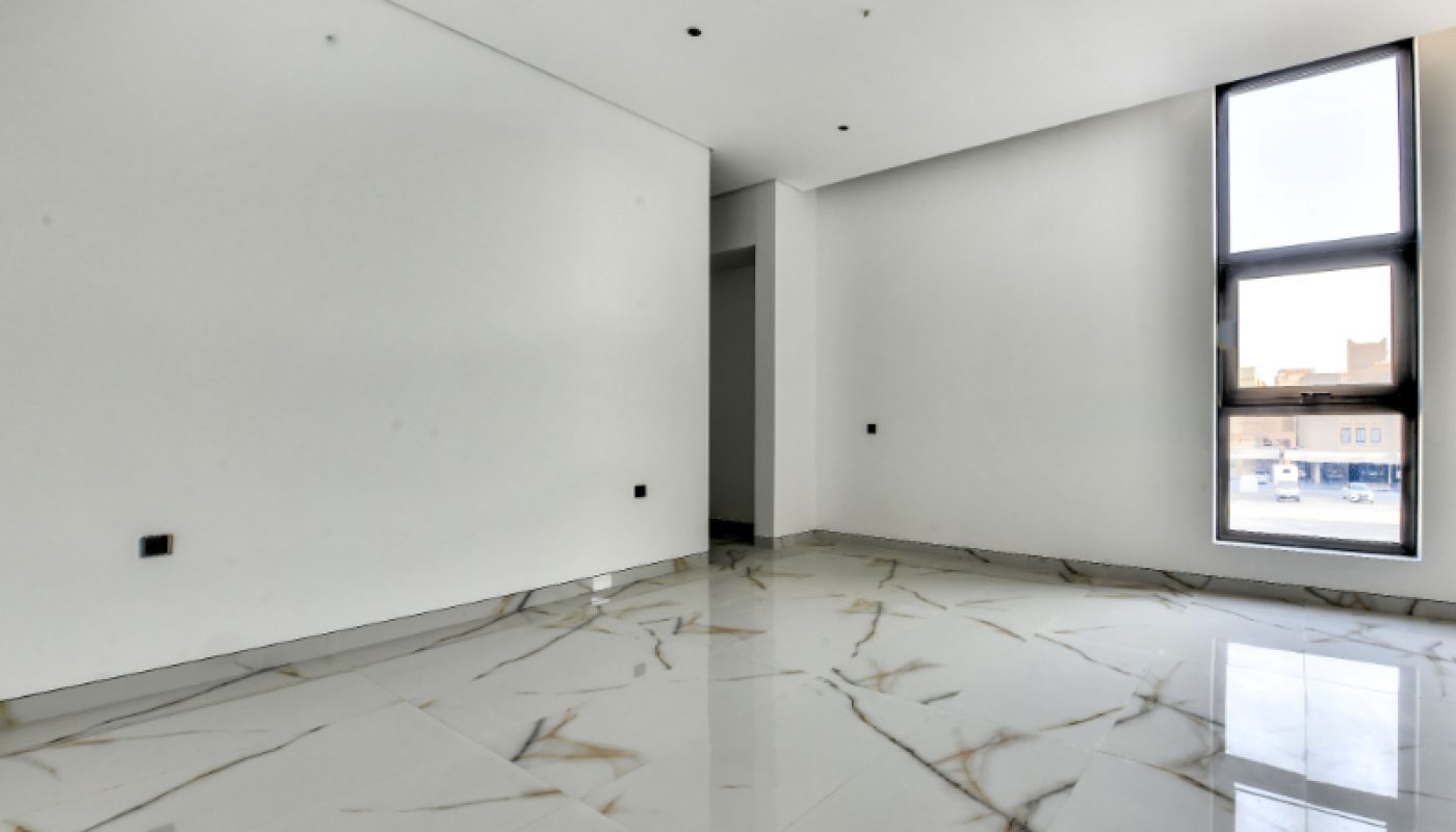 Empty modern room with white walls, large glossy marble floor tiles, recessed lighting, and a tall window letting in natural light.