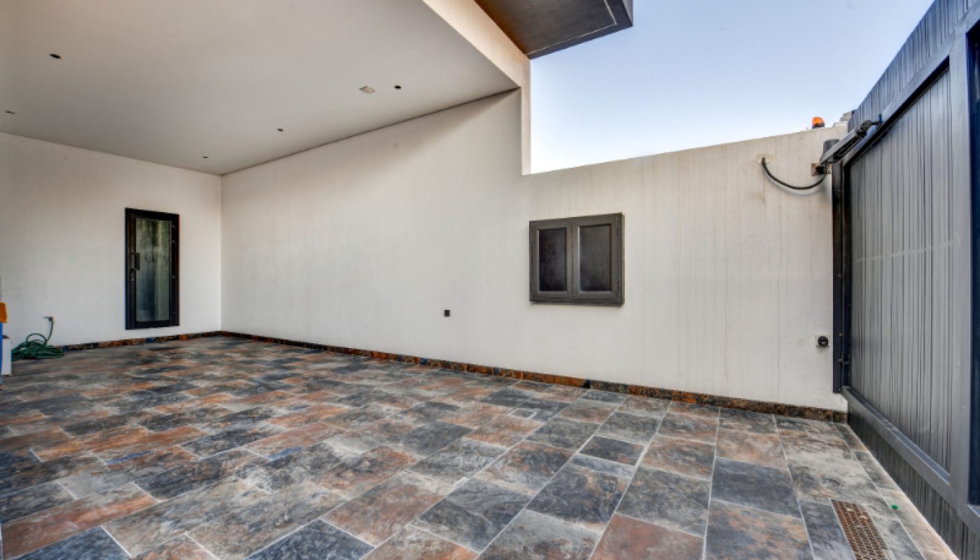 Covered outdoor area with tiled flooring, white walls, a small window, a black door, and a large black gate on the right.