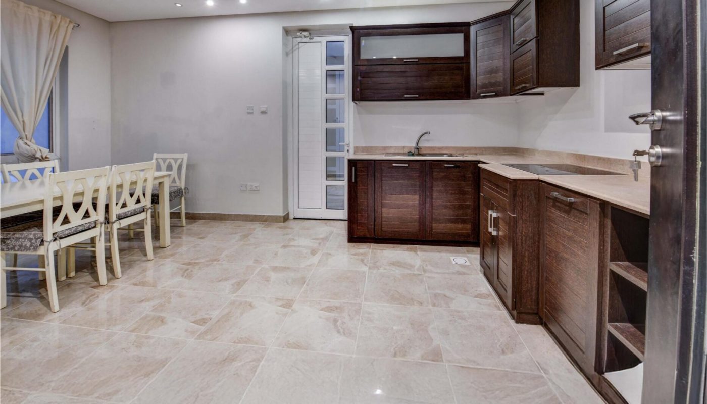 Modern kitchen with dark wood cabinets, beige tile flooring, stainless steel appliances, and a dining area with six white chairs and a table by the window.