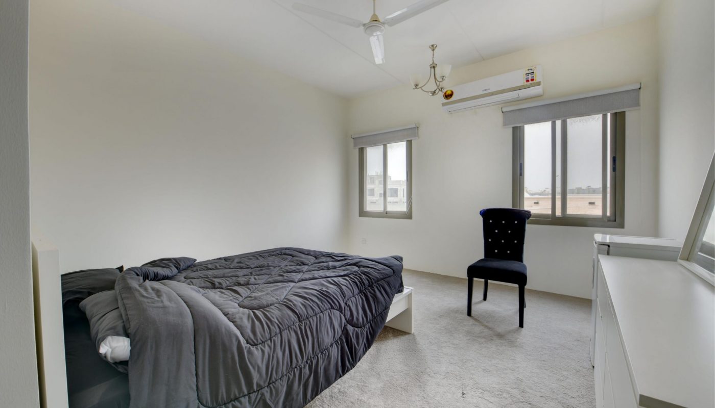 Minimalist bedroom with a single bed, black chair, dresser with mirror, ceiling fan, two windows, and an air conditioner.