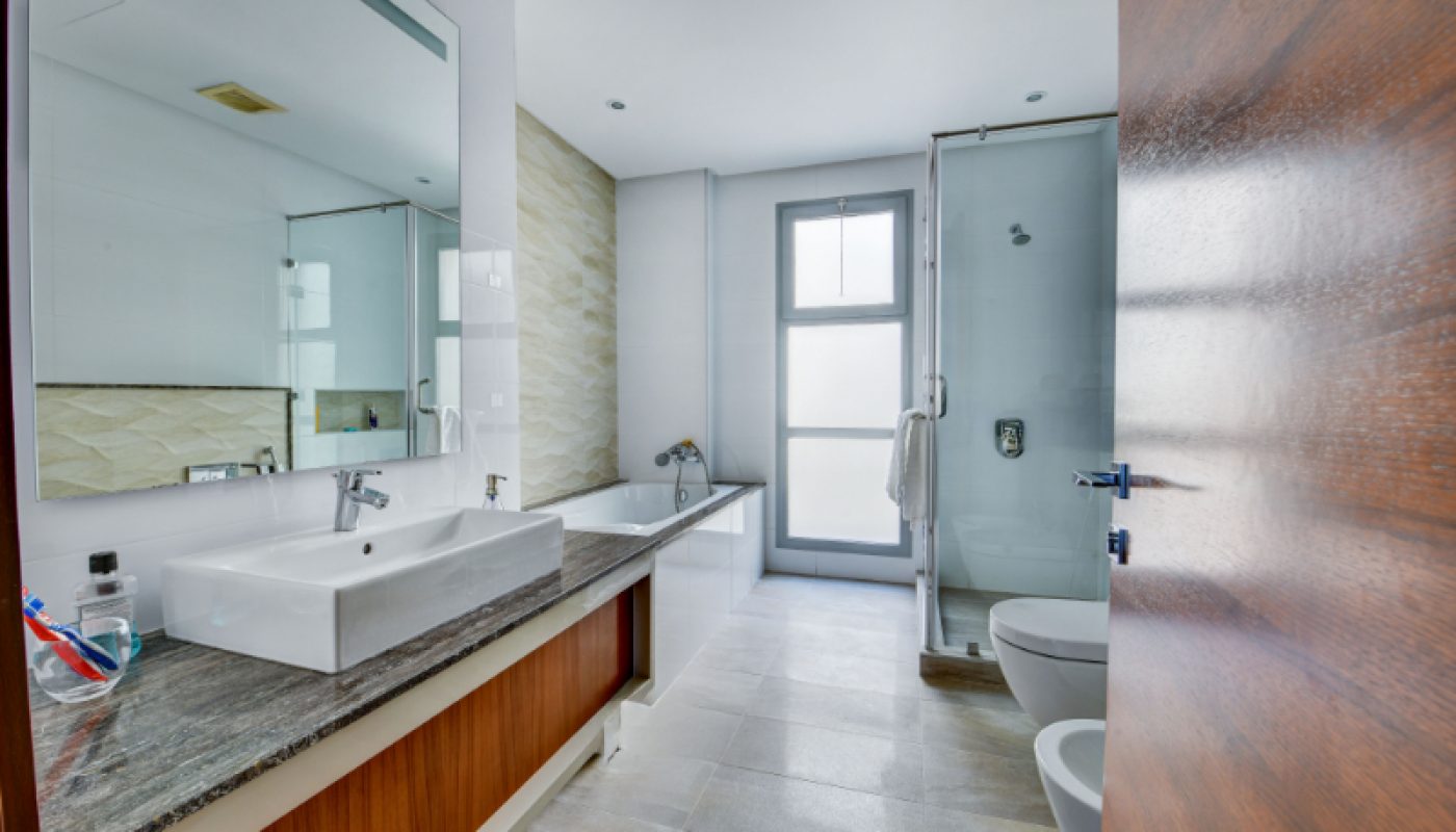 Modern bathroom with a double sink vanity, bathtub, glass-enclosed shower, toilet, bidet, and large window providing natural light.