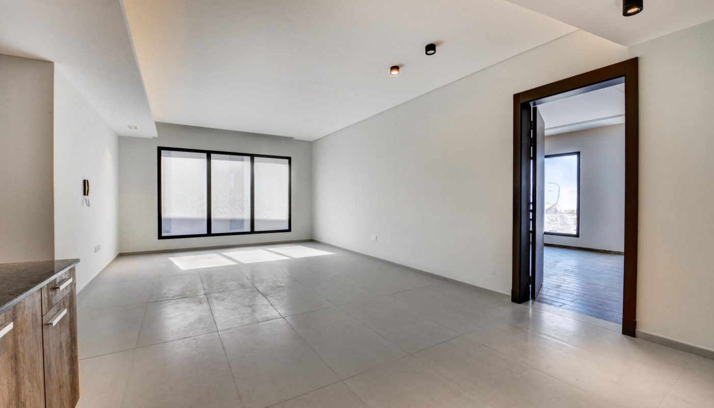 Empty modern room with large windows, light-colored tiled floor, white walls, recessed lighting, and an open doorway leading to another room with darker flooring.