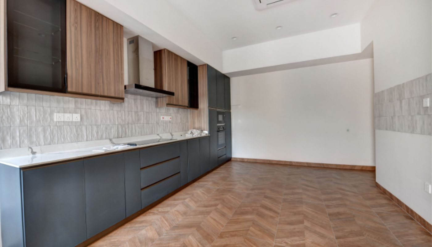 Modern, unfurnished kitchen with built-in cabinets, tiled backsplash, wooden flooring, and a ceiling air conditioning unit. The room is empty and spacious with neutral tones.