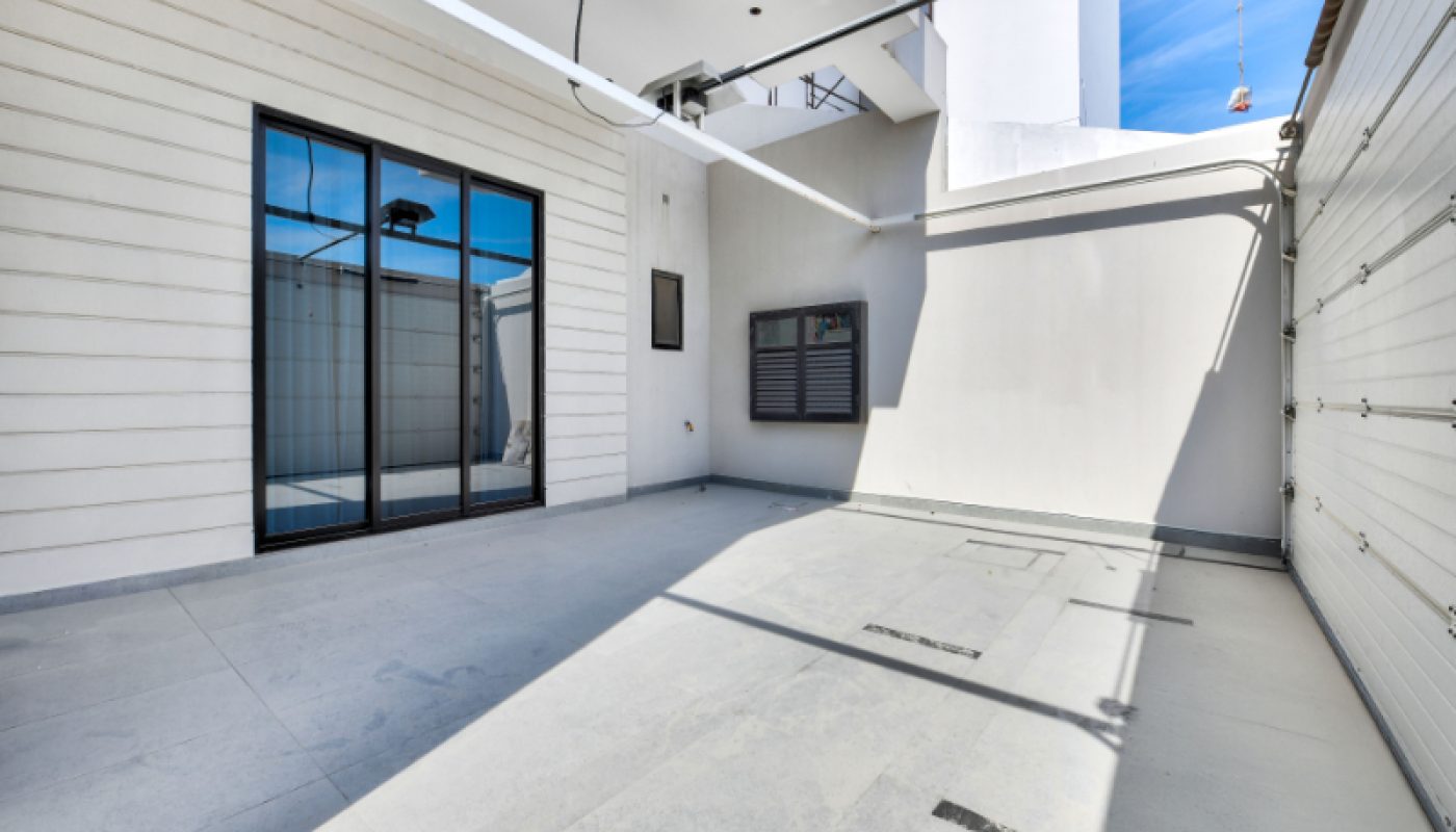 Spacious, modern garage with tiled floor, large windows, white walls, and a closed garage door; sunlight casts shadows across the area.