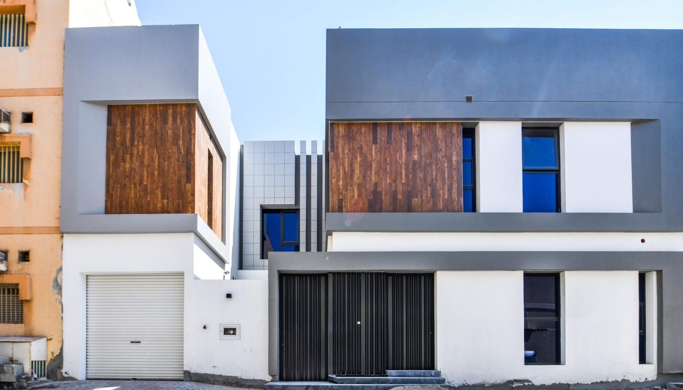 A modern two-story building with a flat roof, large windows, wooden panels, and a garage door, adjacent to another building with a beige facade.
