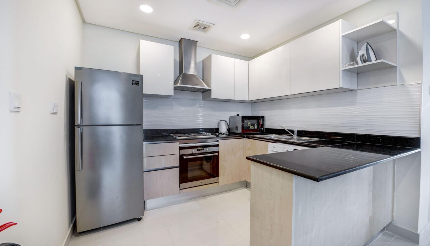 Modern kitchen with stainless steel refrigerator, built-in oven, stove, microwave, and white cabinets; L-shaped countertop with sink and dish rack.