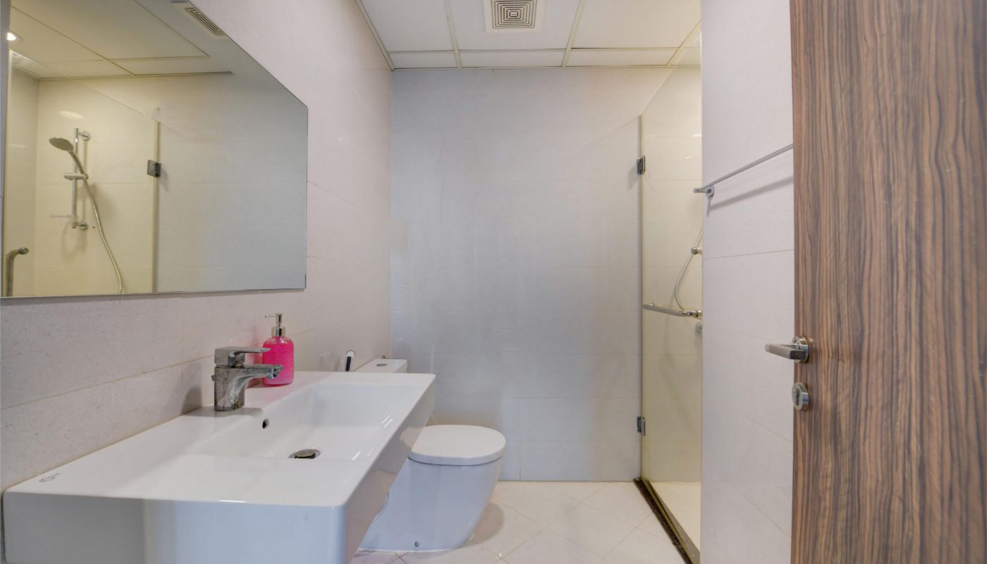 Modern bathroom with a wall-mounted sink, toilet, large mirror, wooden door, towel rack, and a glass-enclosed shower area.