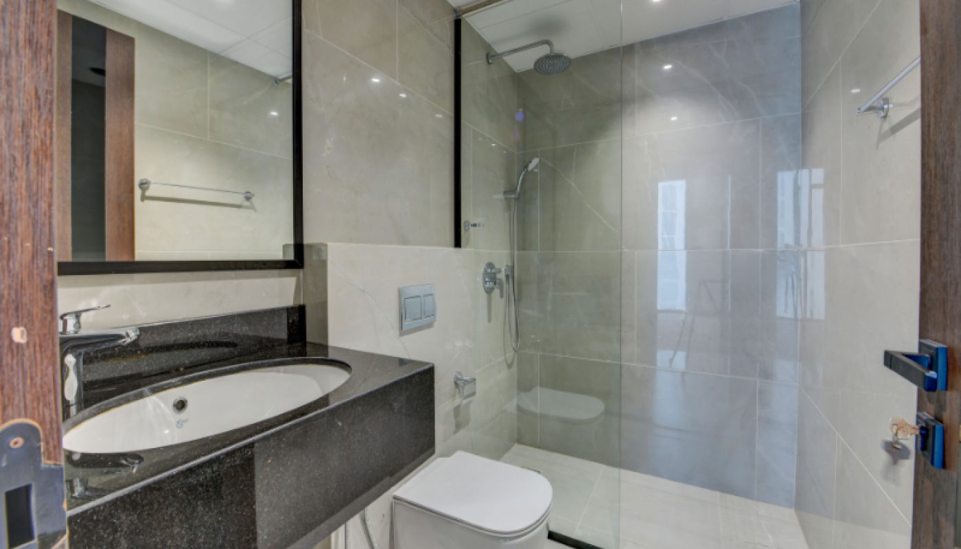 Modern bathroom with beige tiles, a glass-enclosed shower, wall-mounted toilet, black countertop sink, and a large mirror.