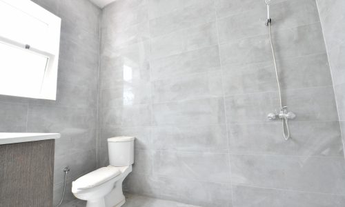 A bathroom located in a villa, with grey tiled walls and a toilet.