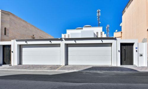 A white garage with a black door is part of a luxurious villa for sale in Muqsha.