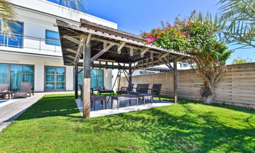 Modern backyard patio area with pergola and outdoor furniture in a landscaped garden of a 5BR Villa for Rent on Tala Island.