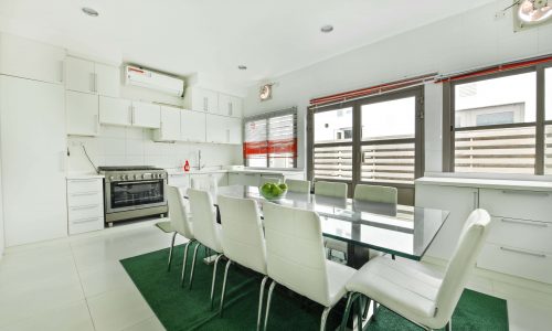 Modern kitchen interior with white cabinets, stainless steel appliances, and a dining area with a glass table and white chairs in a 5BR Villa on Tala Island for rent.