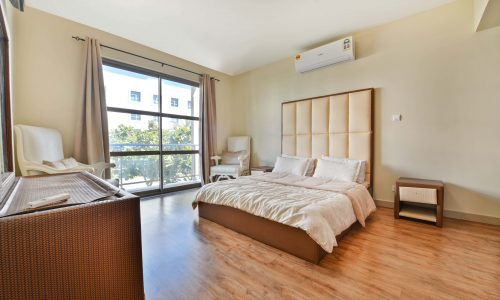 Bright and airy bedroom in a 5BR Villa for Rent, with a large bed, wooden floor, and an open balcony door.