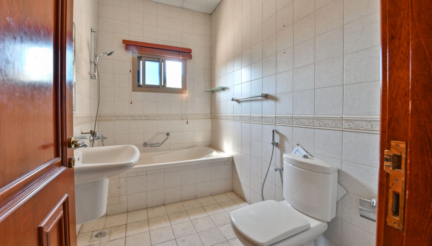 A clean, bright bathroom interior featuring a bathtub, toilet, sink, and a window, with white and beige Auto Draft tiled walls.