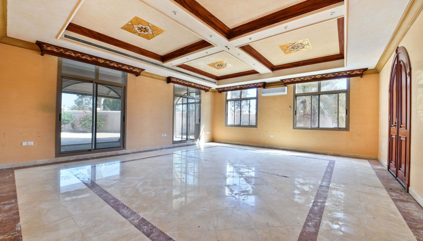 Empty luxury room with shiny marble floors, large windows, and ornate ceiling details.