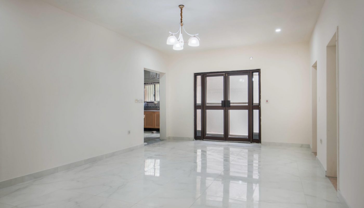 Empty room with white marble floor, cream-colored walls, ceiling light fixture, glass double doors, and two open doorways leading to other areas.