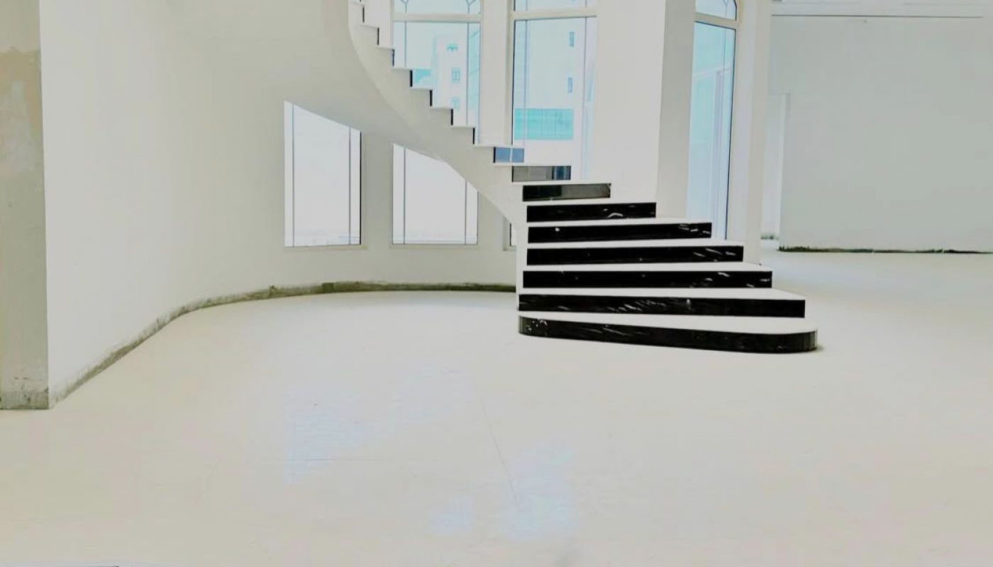 A modern, minimalistic white interior with a black spiral staircase and arched windows allowing natural light to enter.