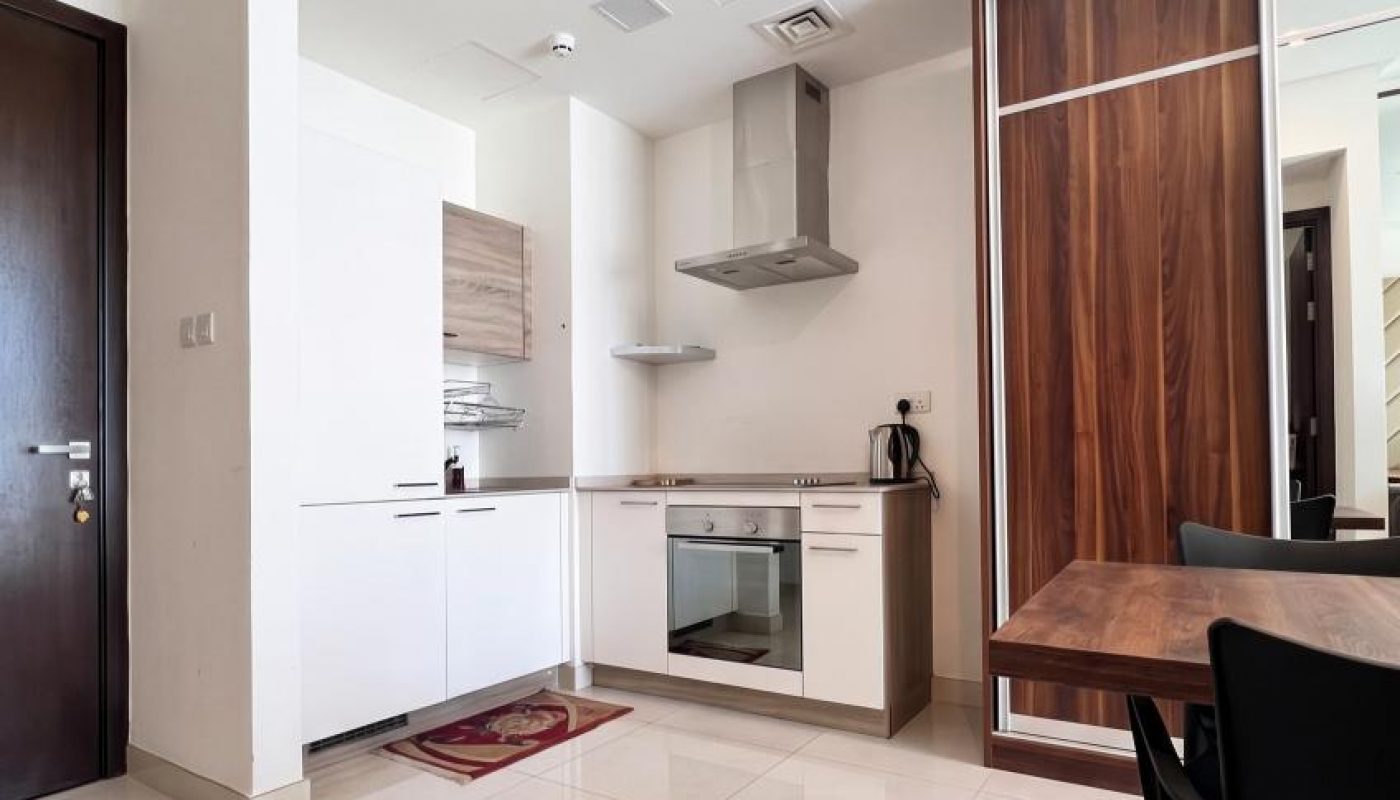 Modern kitchen with white cabinets, built-in appliances, a brown dining table with black chairs, and tiled flooring. Wood accents on cabinetry and wall.