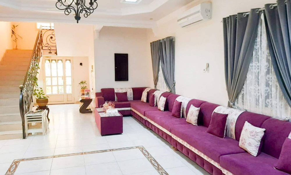 A luxurious living room with purple couches and a staircase in an 8BR Villa for Sale in Samaheej.