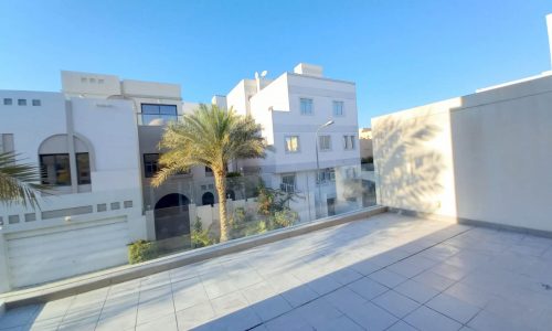 A luxury villa for rent in Saar with a balcony offering views of palm trees and the surrounding buildings.