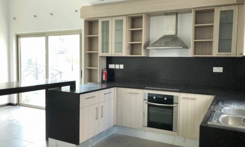 A kitchen with white cabinets and black countertops in a lavish 4BR villa for rent in Hamala.