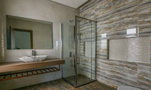 A modern bathroom with a glass shower stall and wooden floors in a unique 3BR apartment for sale in Sanad Area.