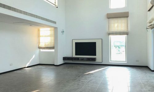 An empty living room with large windows and a tv in a lavish villa.