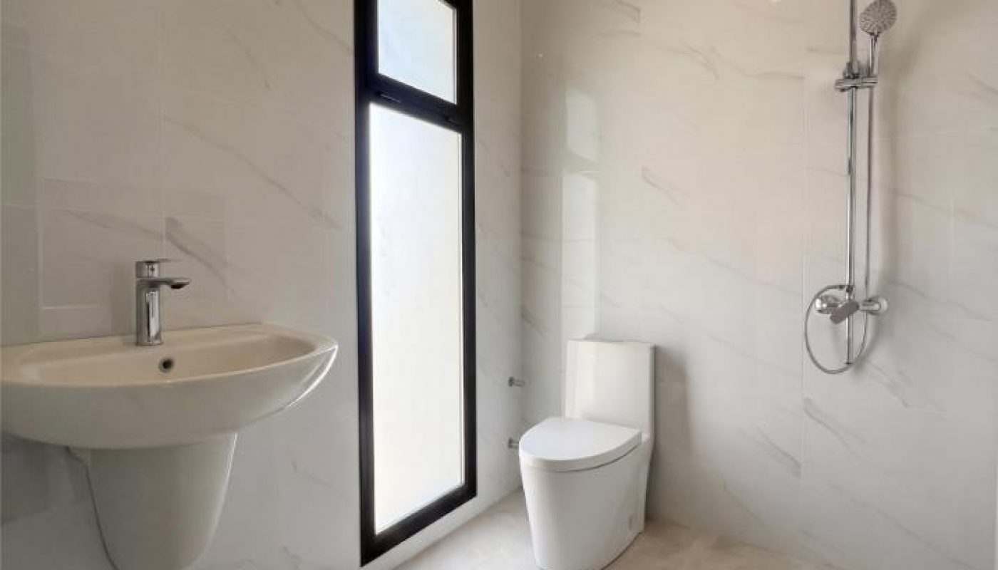 Modern bathroom with a wall-mounted sink, frosted window, white toilet, and a rain shower head on marble-style tiles.