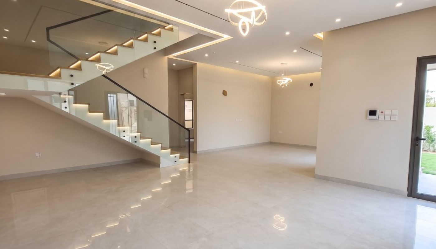 Spacious modern living room with marble floors, glass staircase, recessed lighting, and large windows letting in natural light.