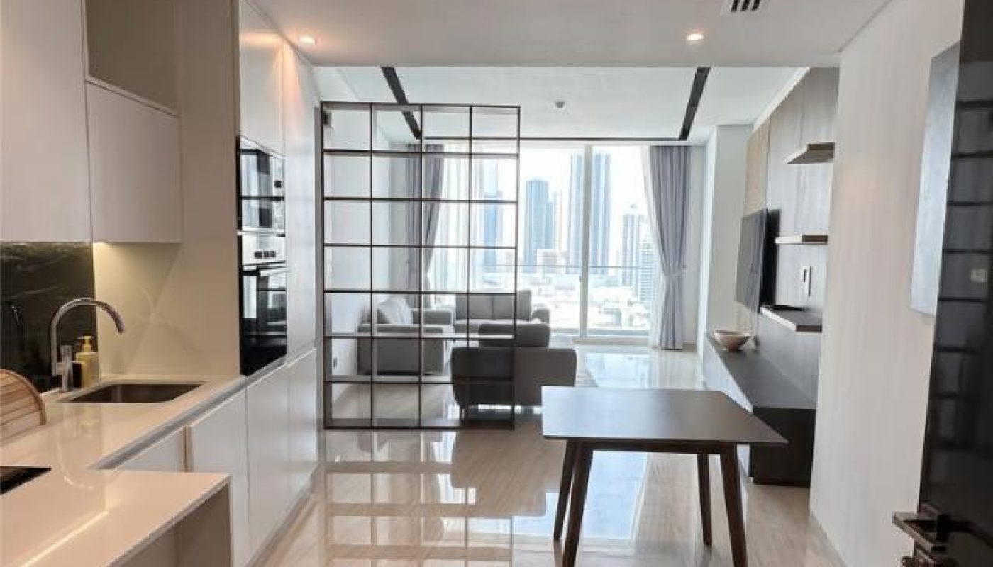 Modern apartment interior with open kitchen, dining table, and living area separated by glass partition; large windows offer a city view.