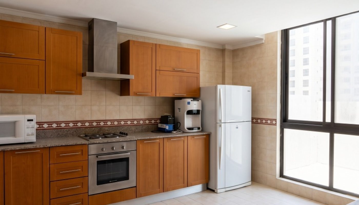 Modern kitchen with wood cabinets, stainless steel appliances, a white refrigerator, microwave, coffee maker, and large window allowing natural light.