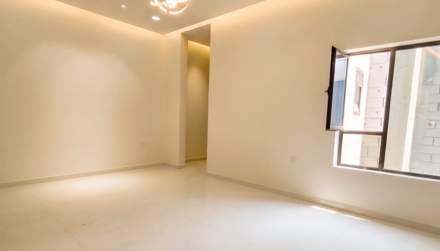 Empty, well-lit room with white walls and floors, recessed lighting, a modern ceiling fixture, and an open window letting in natural light.