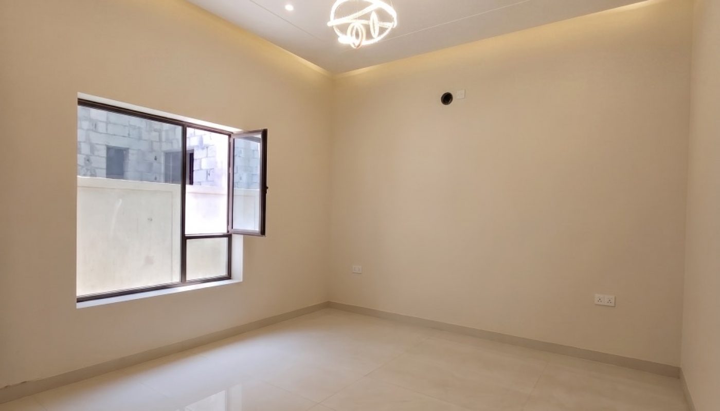 Empty room with cream-colored walls, tiled floor, a large window, ceiling lights, and a modern chandelier fixture.