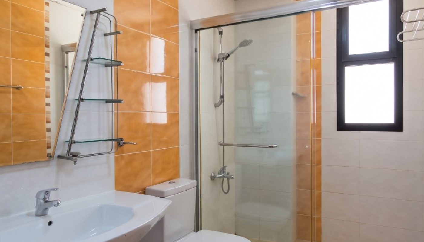 Modern bathroom with a wall-mounted sink, toilet, glass-enclosed shower, orange and white tiles, and a window.