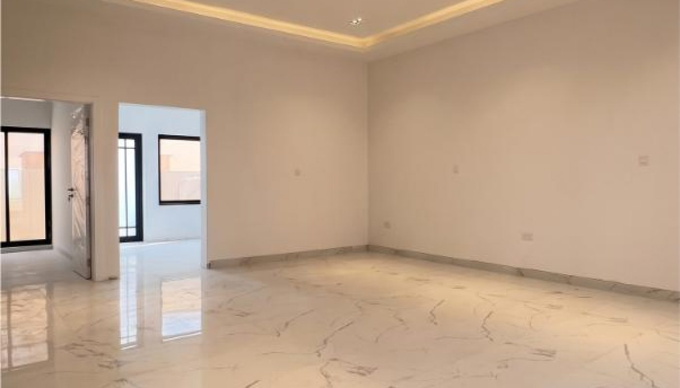 Spacious empty room with white marble floors, recessed ceiling lights, and large windows letting in natural light.