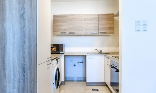 A small kitchen with exceptional facilities such as a washer and dryer, available in a 1BR flat for rent in Juffair.